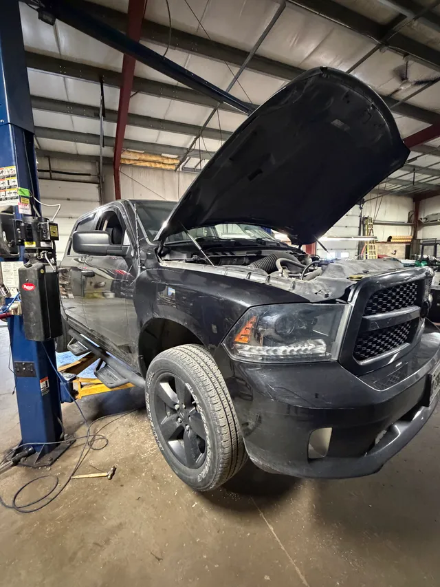 Dark pickup with its hood open inside the workshop
